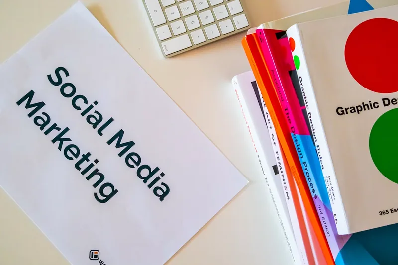 Social media marketing plan on a desk beside graphic design books and a keyboard